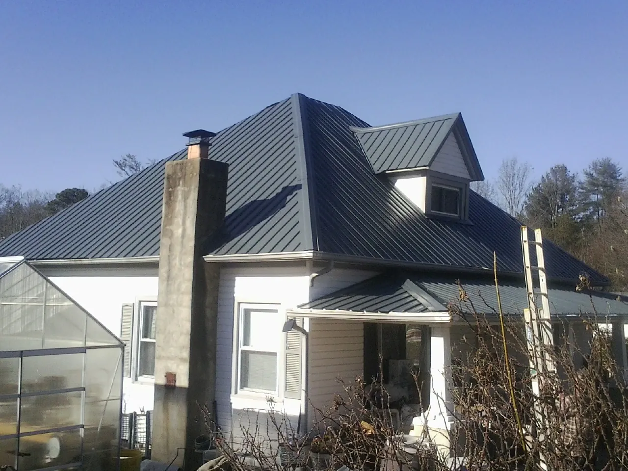 Dark blue standing seam metal roof on a white farmhouse with dormer — Slate & Tile Roof Repair by Roofing Brothers in Hamlet