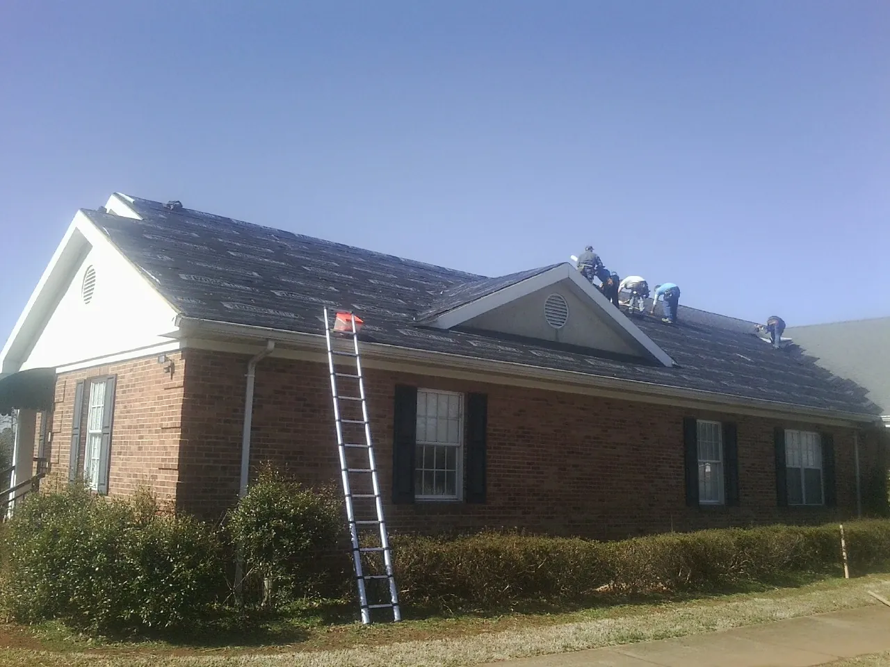 Crew tearing shingles off a brick ranch roof with a ladder set — Metal Roof Repair work by our crew in Hamlet