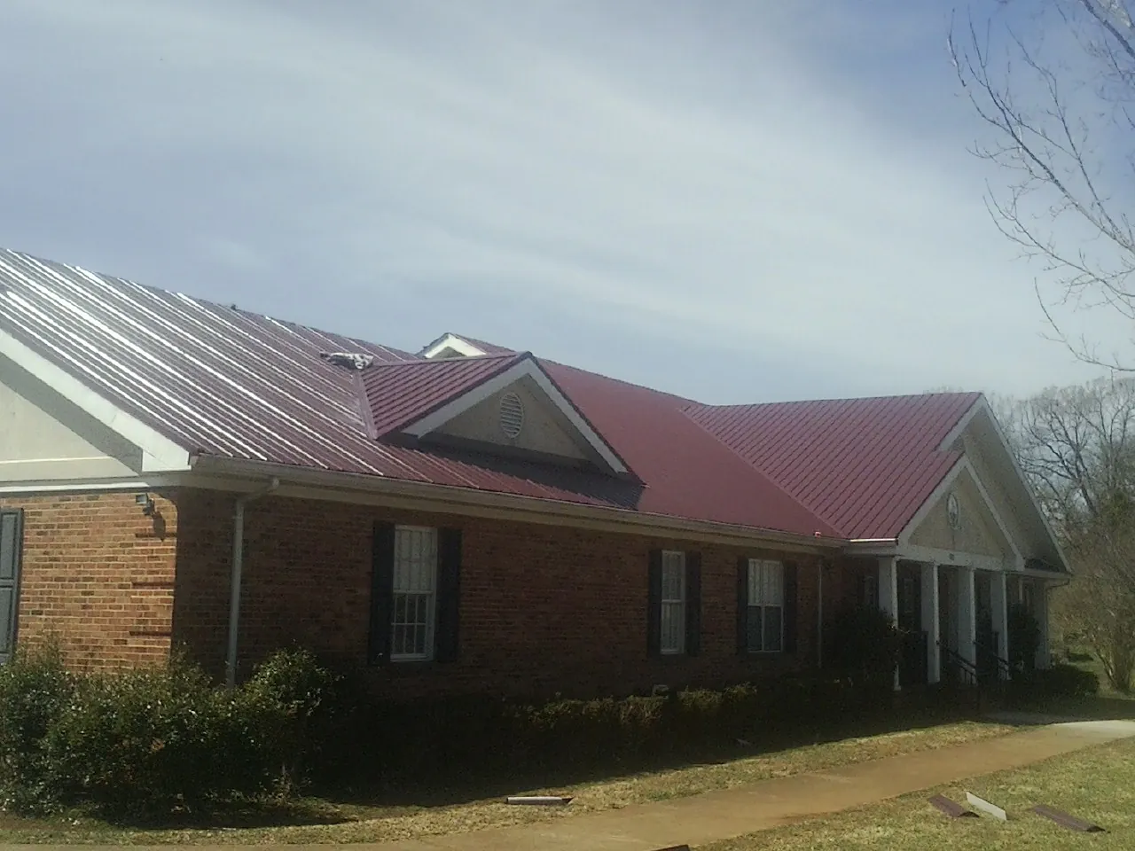 Red metal roof with gabled entries on a long brick building, from a Hail Damage Roof Repair job in Hamlet