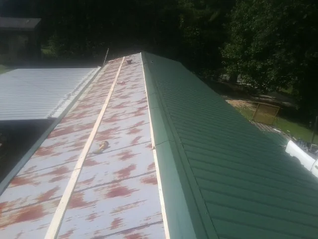 Old rusted panels beside newly installed green metal roofing — Wind Damage Roof Repair by Roofing Brothers in Hamlet