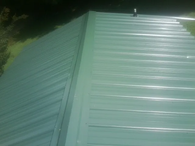 New green metal panels meeting at the ridge of a roof — Flat Roof Repair work by our crew in Hamlet